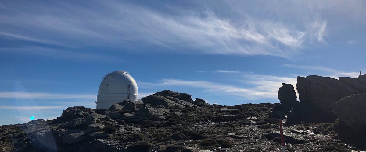 A white dome structure on a rocky hill with sparse vegetation under a clear sky.