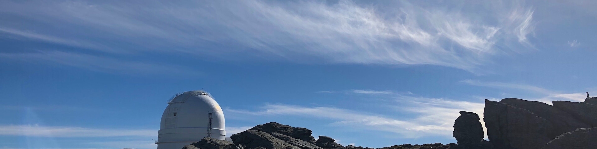 A white dome structure on a rocky hill with sparse vegetation under a clear sky.
