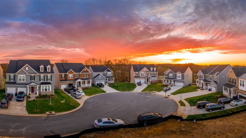 A suburban neighborhood during sunset with houses and cars.