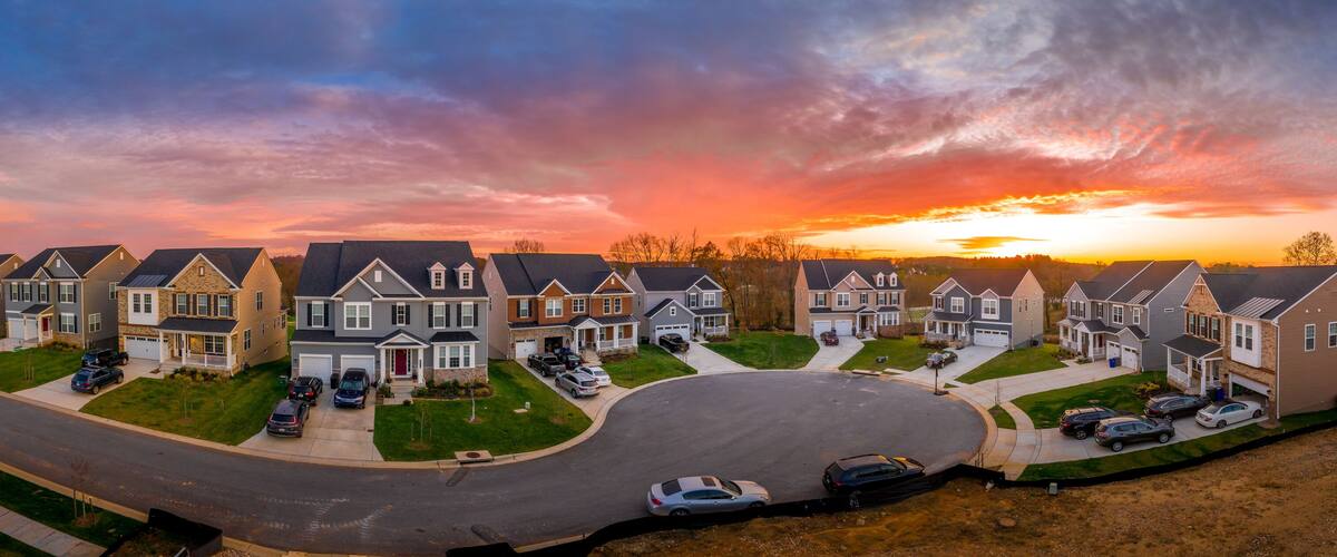 A suburban neighborhood during sunset with houses and cars.
