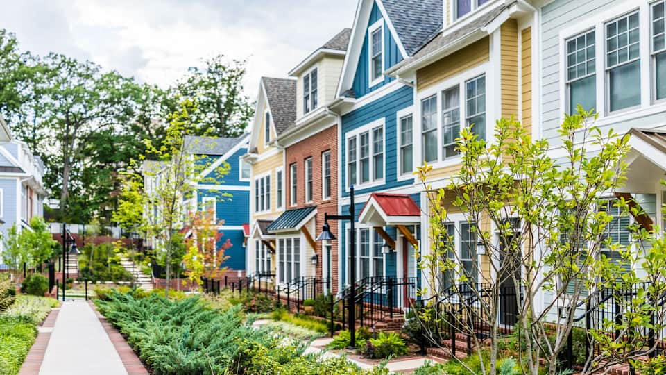 A row of colorful townhouses with a brick pathway and greenery.