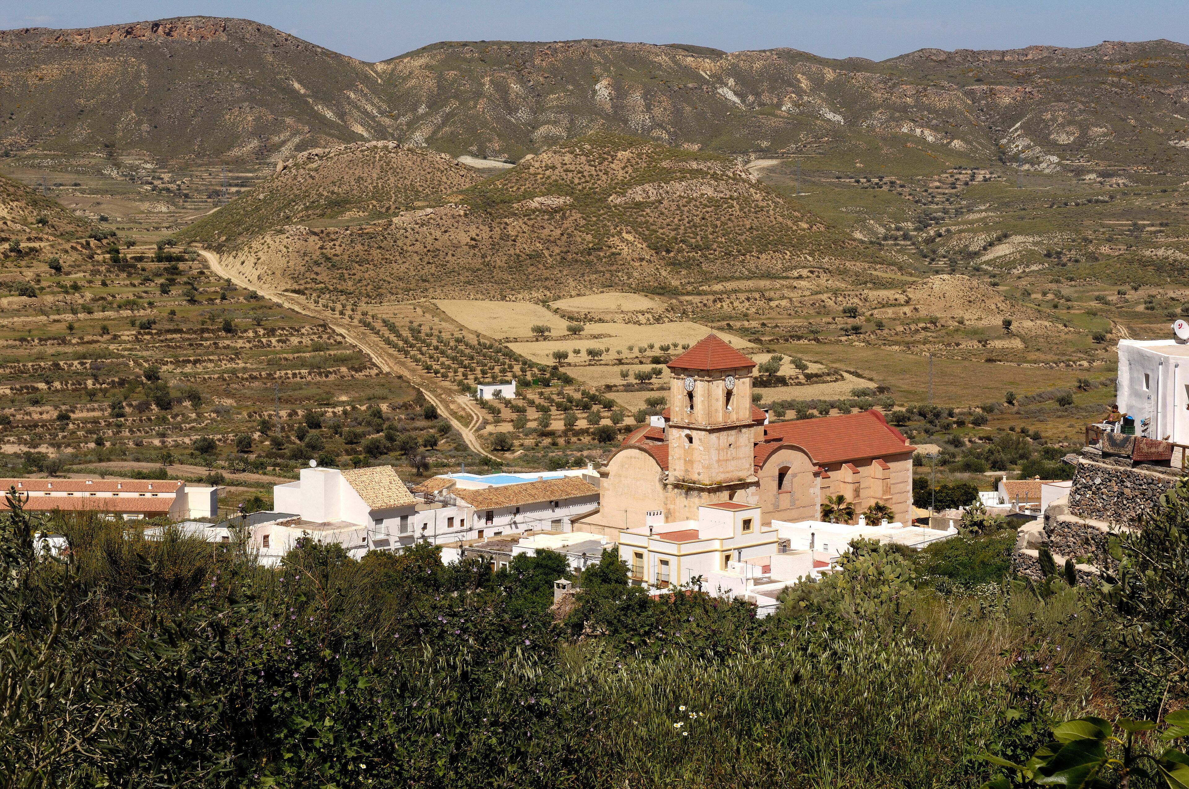 A mountainous landscape with terraced fields, a church with a red roof, and white buildings.