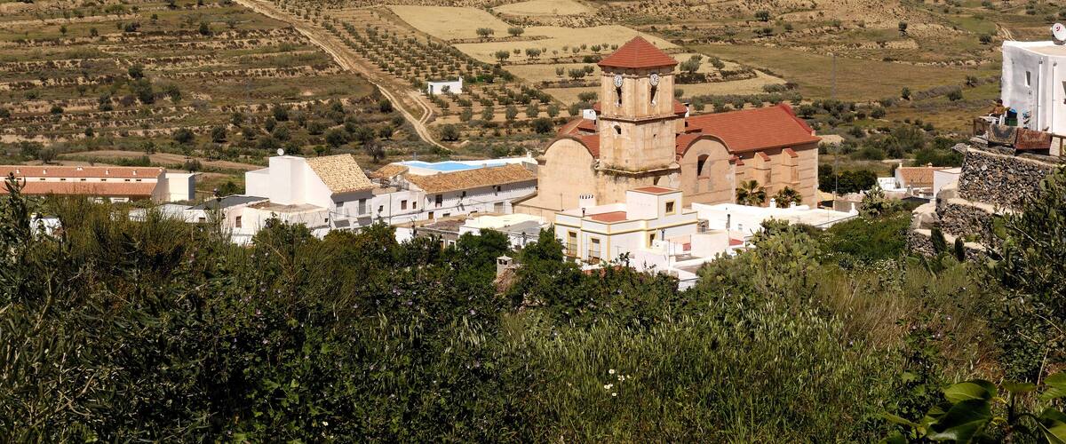 A mountainous landscape with terraced fields, a church with a red roof, and white buildings.
