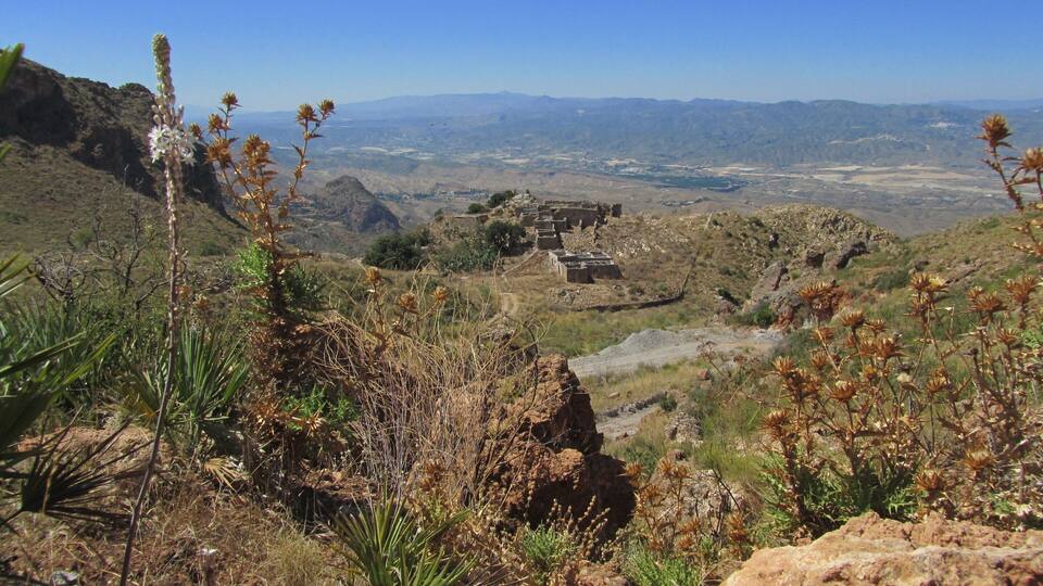 A mountainous landscape with a view of distant mountains, a valley, and a historical ruin.