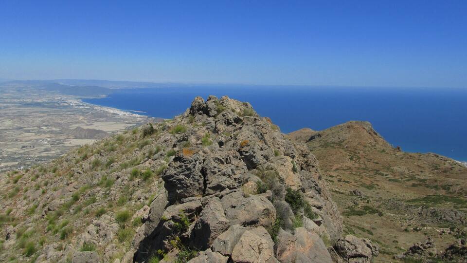A rocky mountain peak with a view of the ocean and a distant coastline.