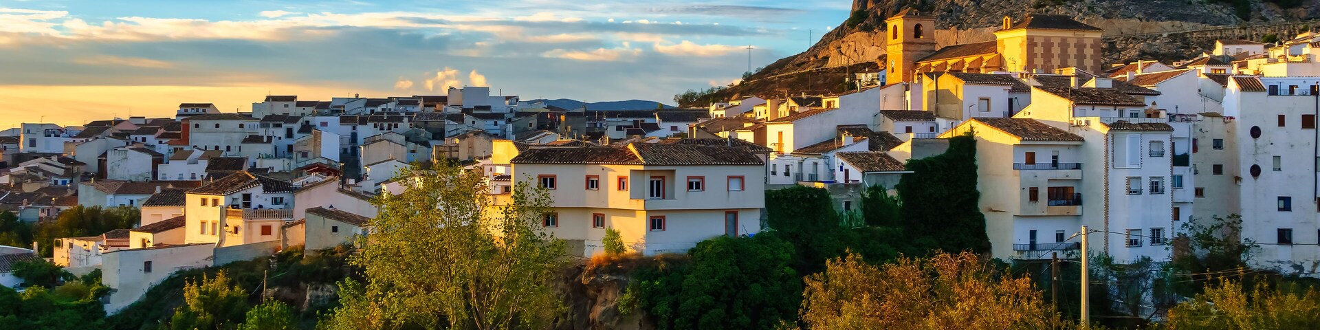 Un pueblo costero con edificios blancos, una iglesia destacada y una colina rocosa al fondo.