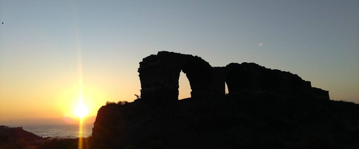 A sunset over a coastal landscape with a prominent rock formation silhouetted against the sky.