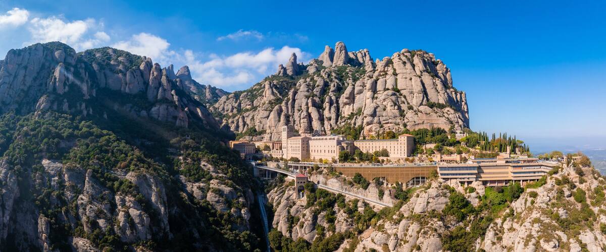 A mountainous landscape with a prominent rocky peak and a building complex on a hillside.