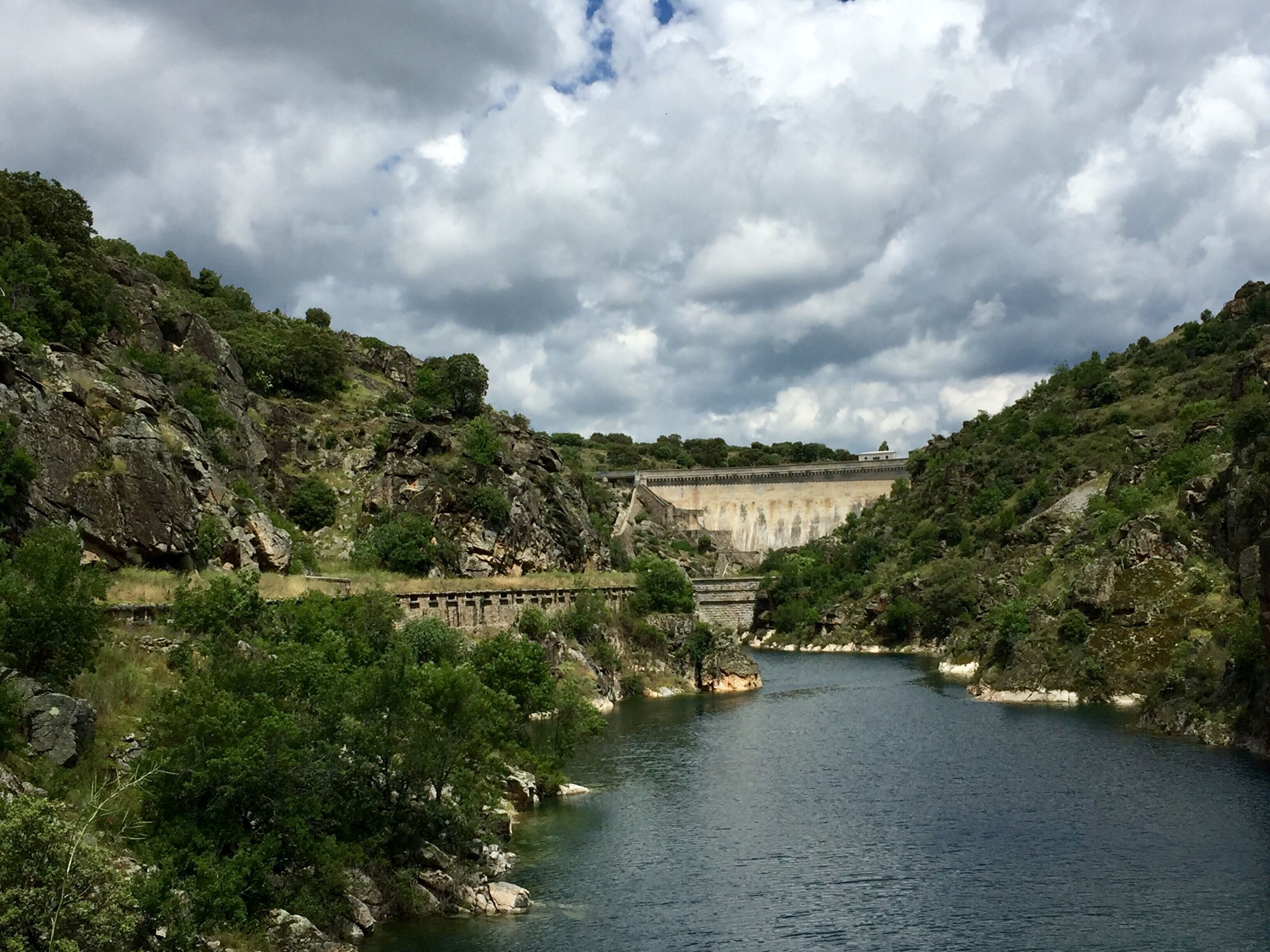 A river flowing through a rocky landscape with a dam in the background.