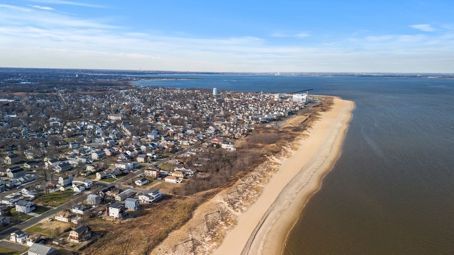 An aerial view of a coastal town with a sandy beach, dense residential area, and a large body of water.