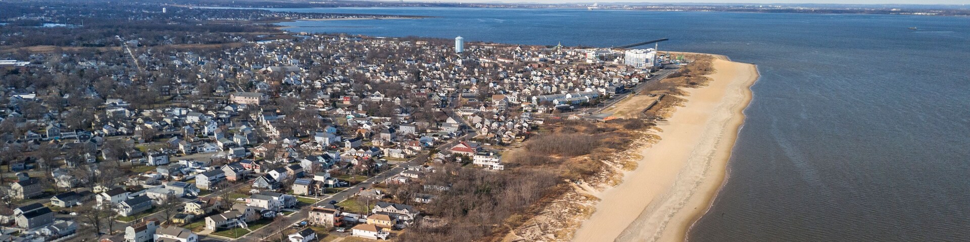 Vista aérea de un pueblo costero con una playa de arena, una zona residencial densa y una extensa masa de agua.