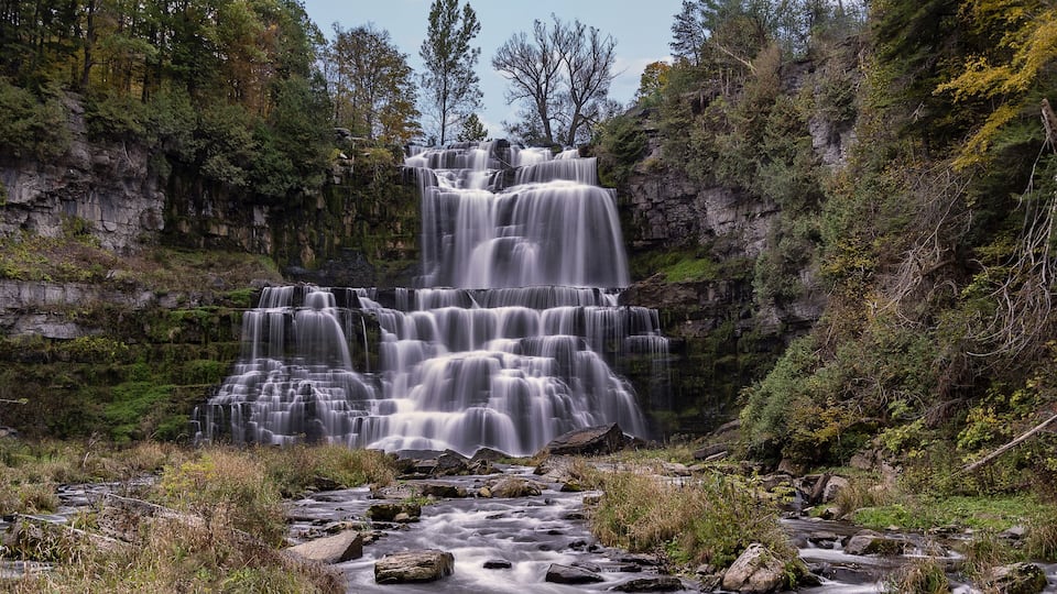 A multi-tiered waterfall surrounded by dense forest and rocky cliffs.