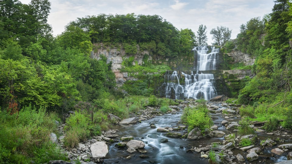 A multi-tiered waterfall surrounded by dense green forest.