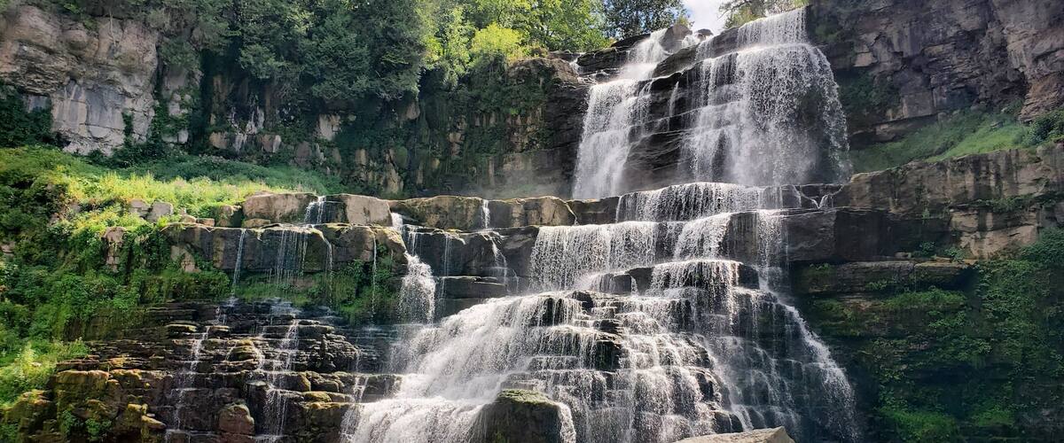 A multi-tiered waterfall cascading over rocky terrain surrounded by lush greenery.