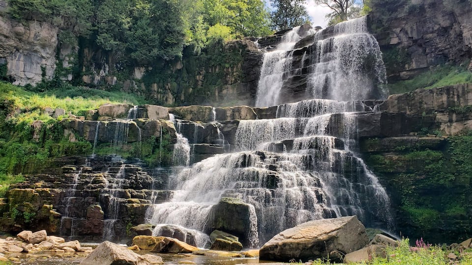 A multi-tiered waterfall cascading over rocky terrain surrounded by lush greenery.