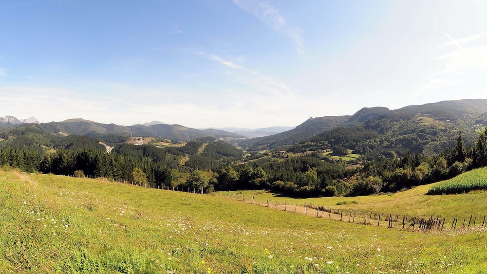 Eine Berglandschaft mit blauem Himmel, sanften Hügeln und einem eingezäunten Feld.