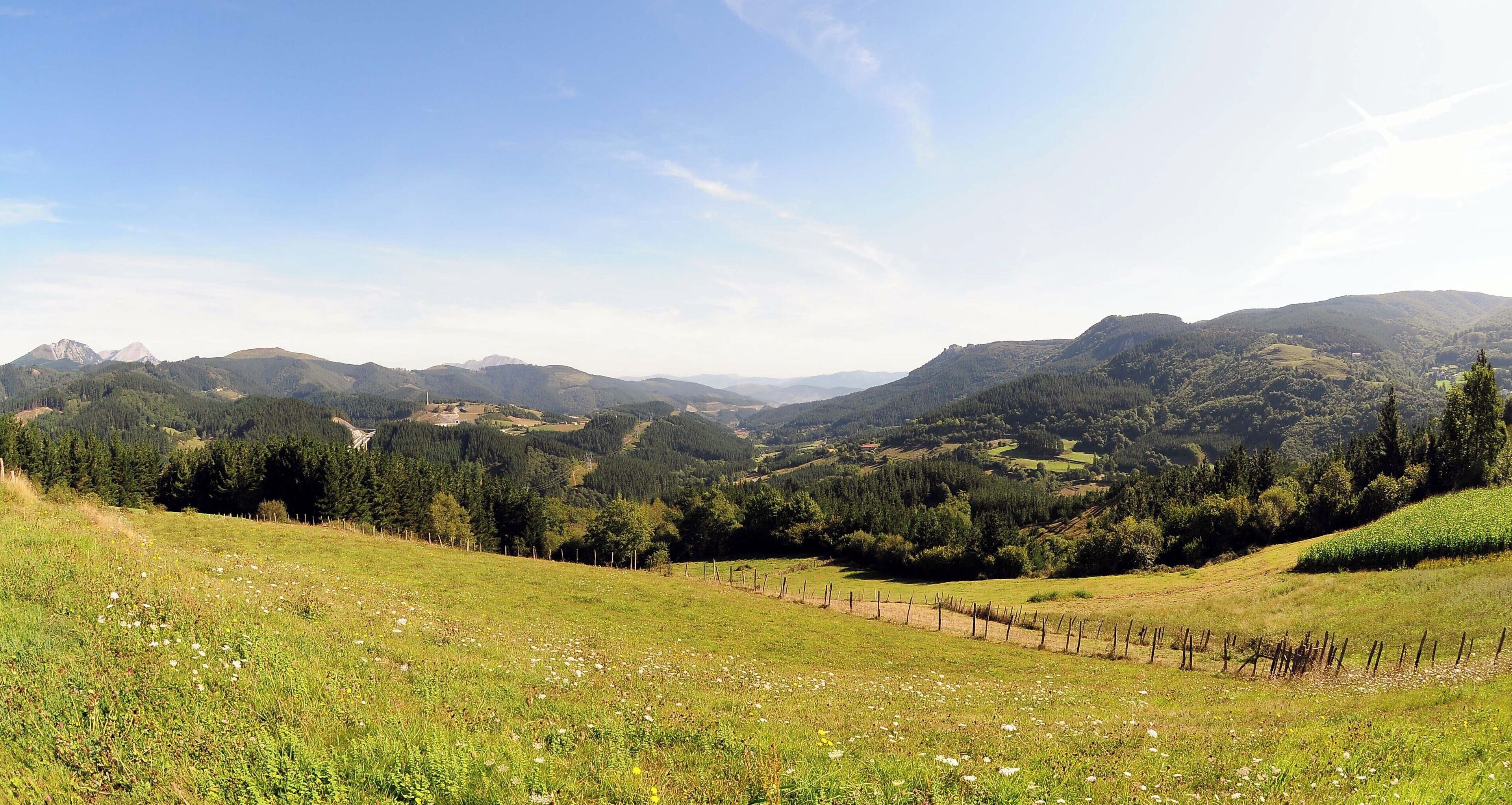 A mountainous landscape with a clear sky, rolling hills, and a fenced field.