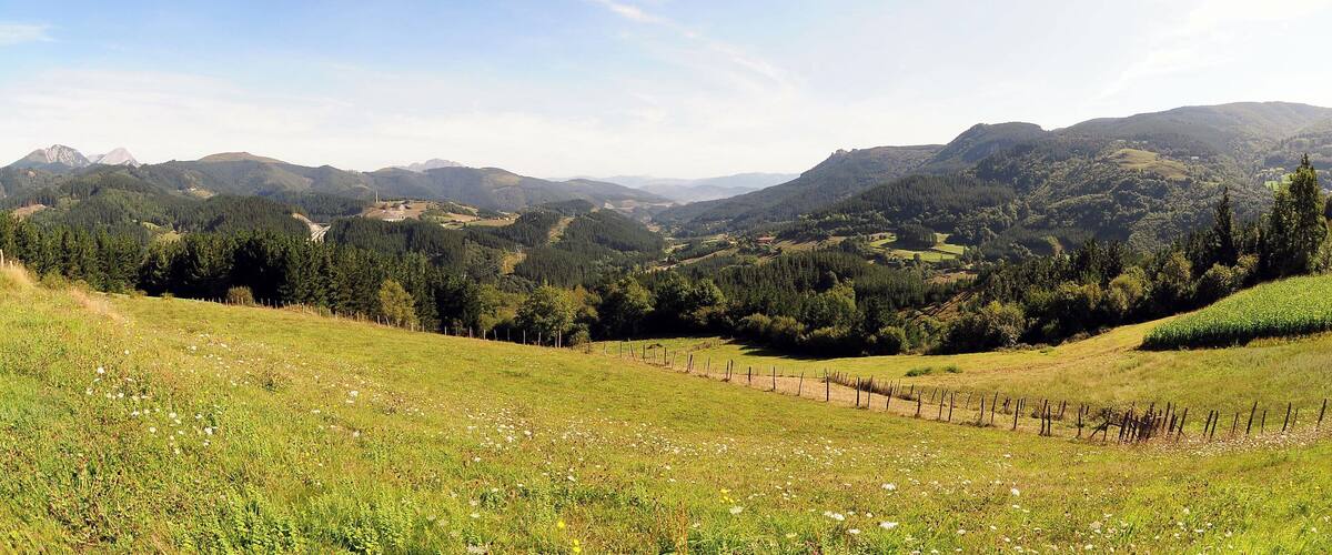 A mountainous landscape with a clear sky, rolling hills, and a fenced field.