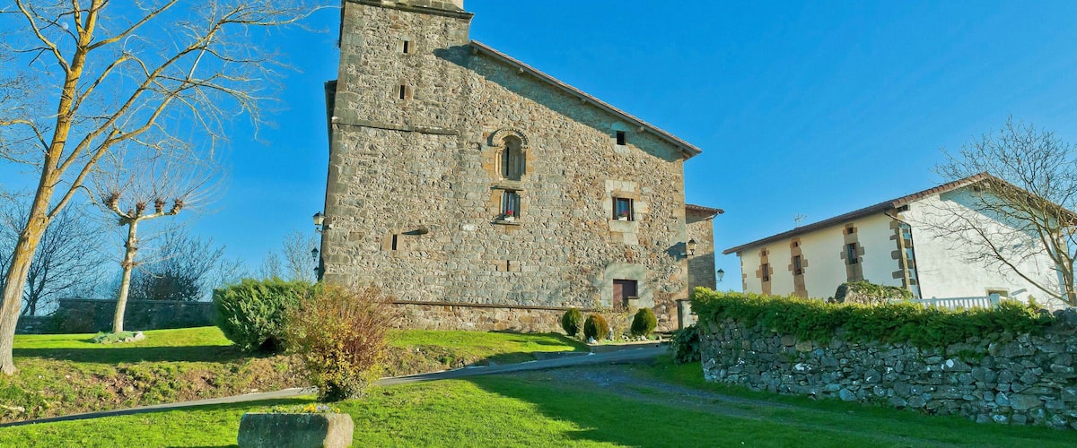 A stone church with a bell tower, surrounded by a stone wall and a grassy area with trees.