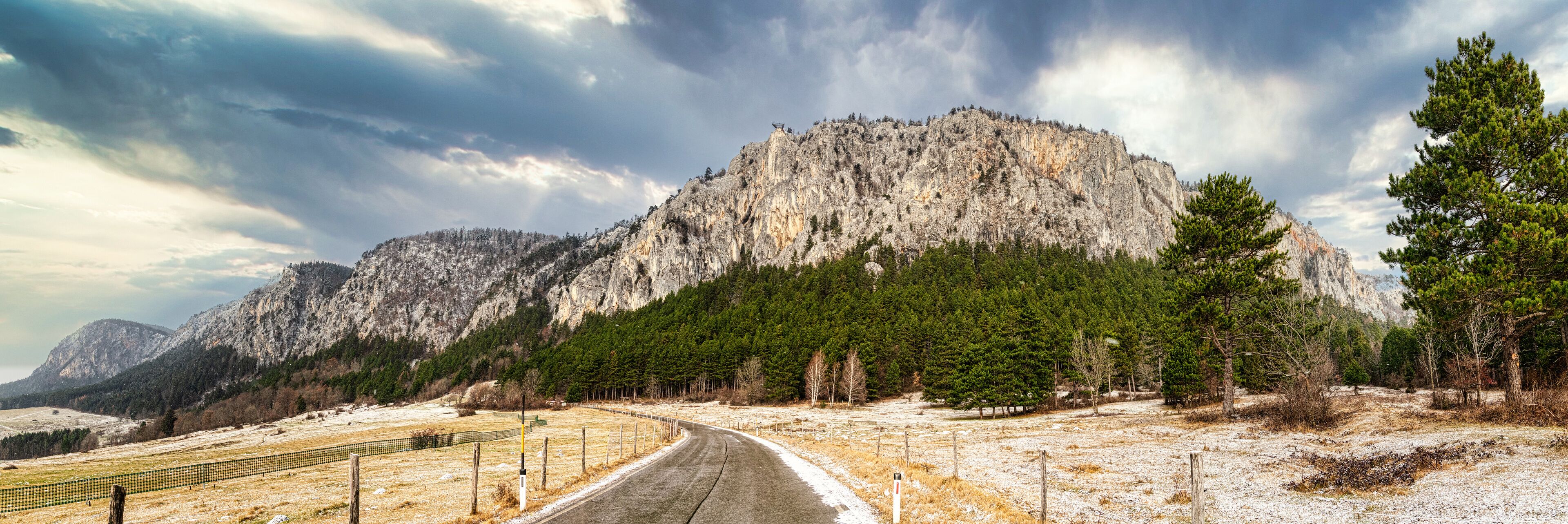 A winding road through a mountainous landscape with a prominent rocky mountain in the background.