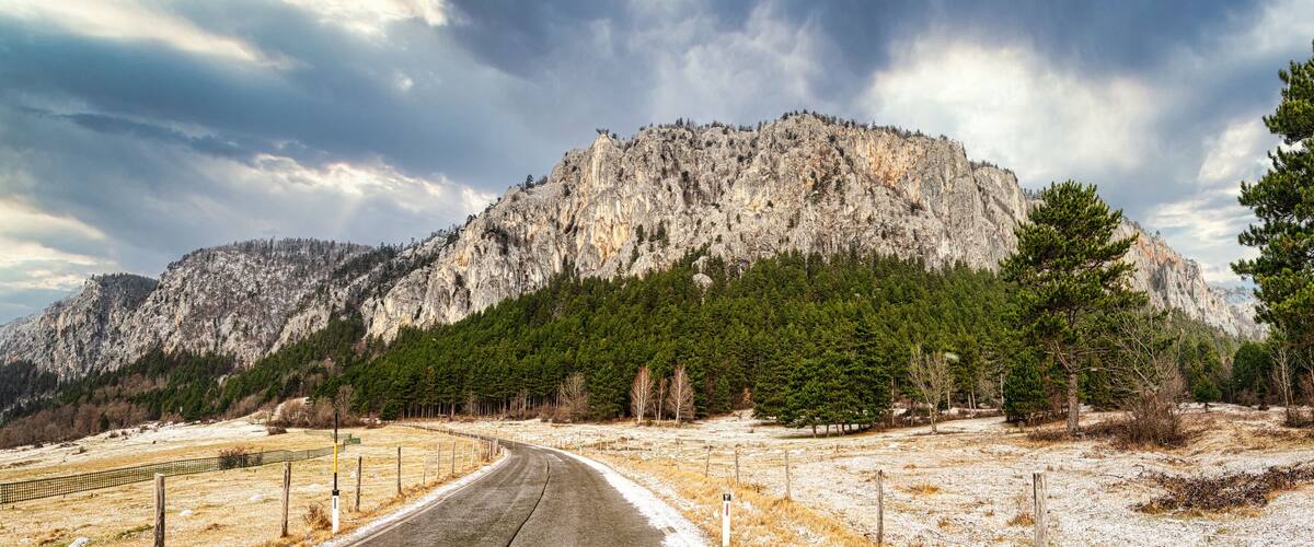 A winding road through a mountainous landscape with a prominent rocky mountain in the background.