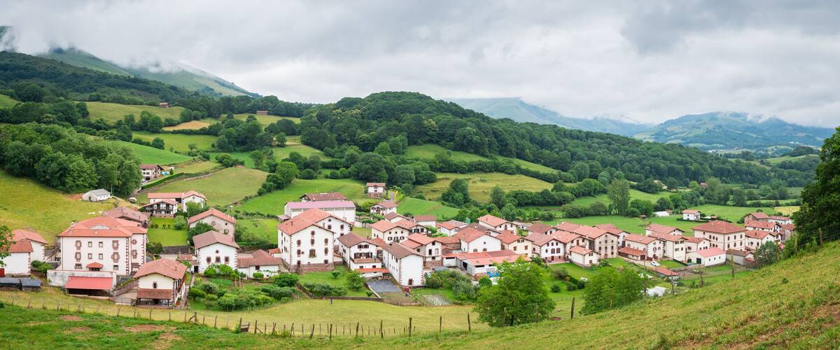 A village with red-roofed buildings nestled in green hills under cloudy skies.
