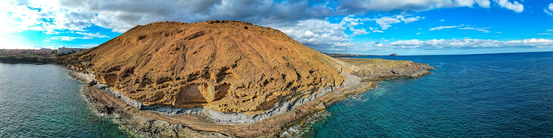 Un paisaje costero con una colina rocosa destacada y aguas azules cristalinas.
