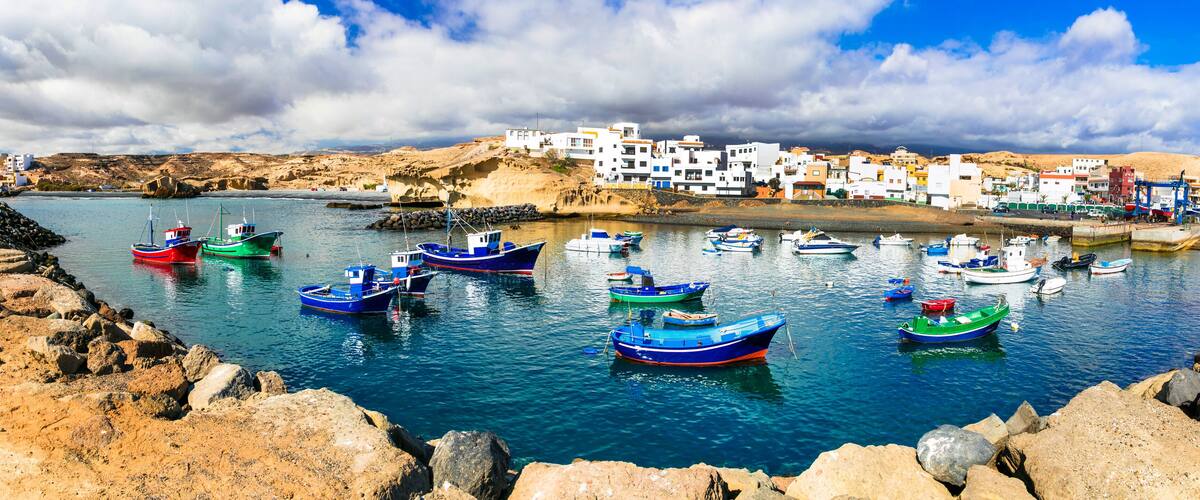 A coastal village with colorful boats docked in the harbor, surrounded by rocky shores and white buildings.