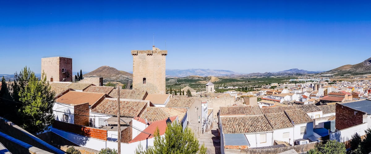 A town with historic buildings, a prominent tower, and a mountainous backdrop.