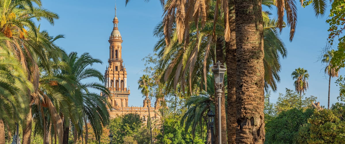 A historic building with a tall tower and spires, surrounded by tall palm trees.