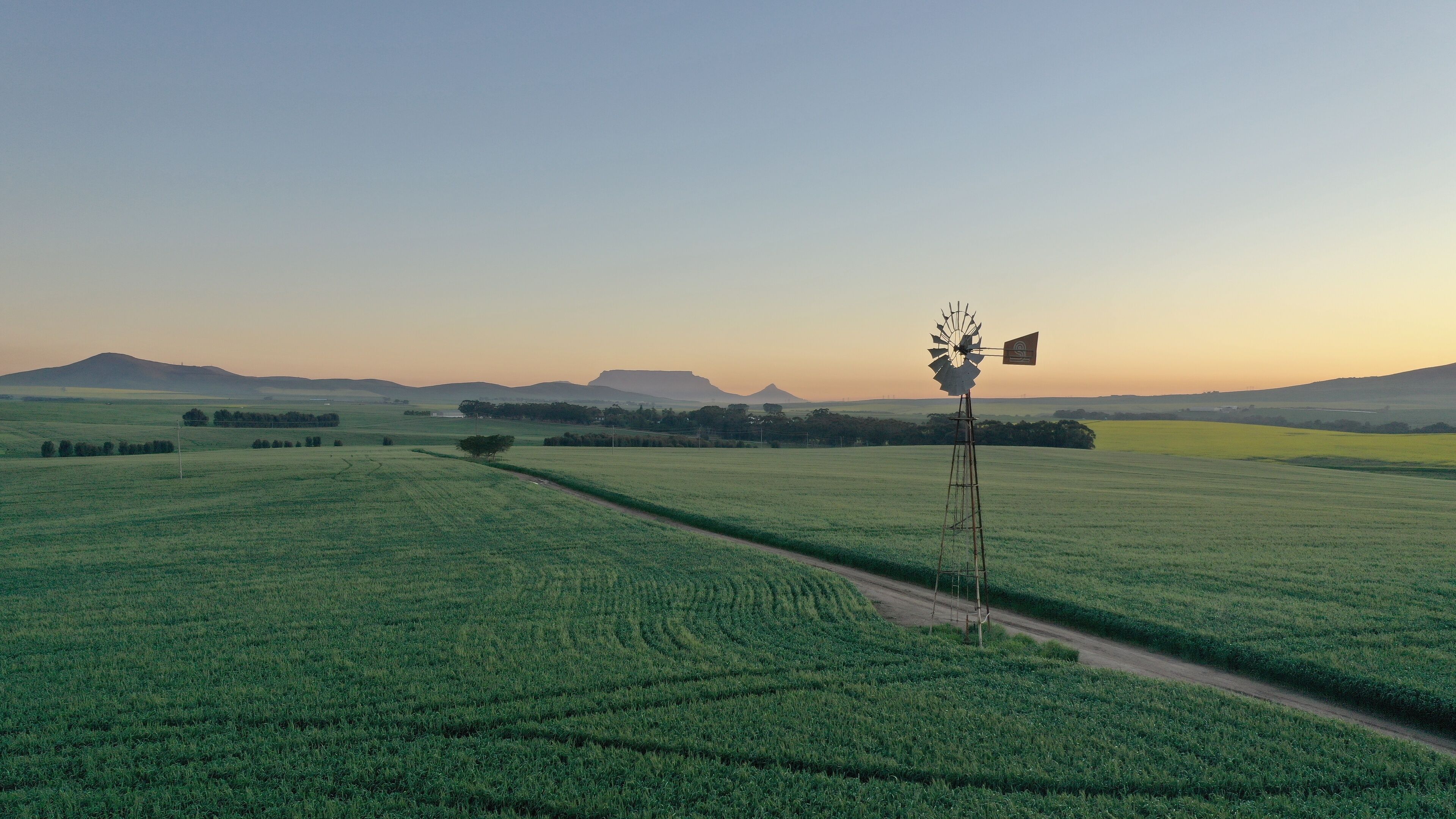 A windmill in a green field with distant hills.