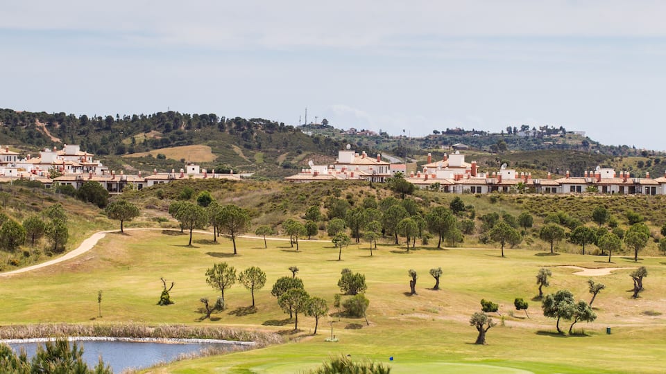 A golf course with a pond, trees, and buildings in the background.