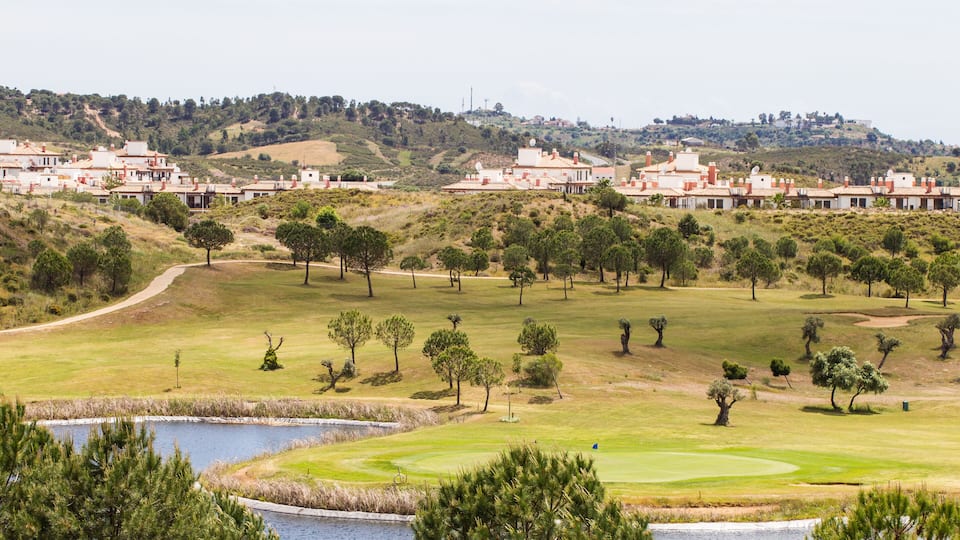A golf course with a pond, trees, and buildings in the background.