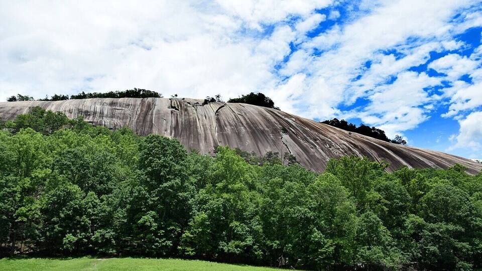 A large rock formation with dense green trees in the foreground.