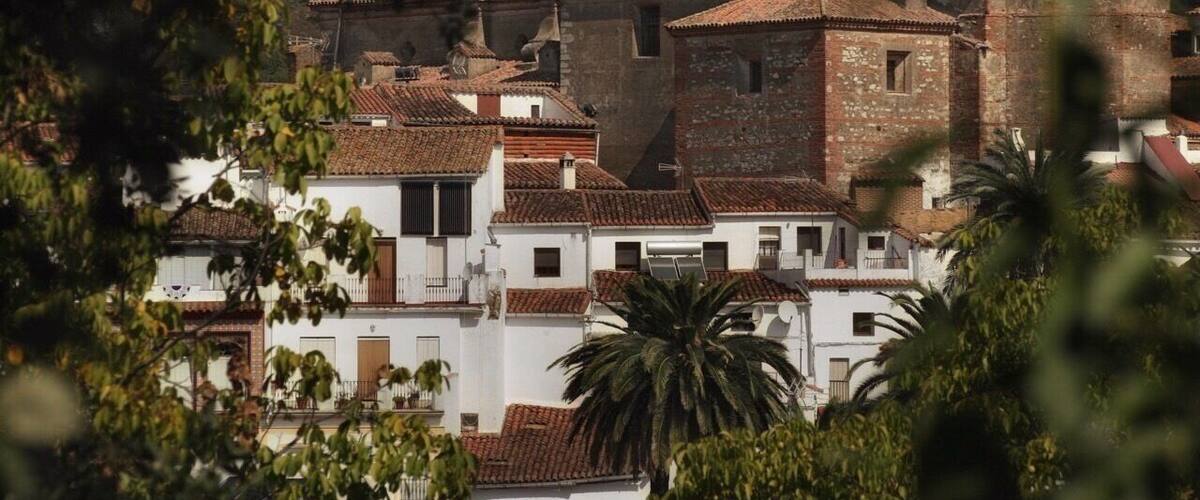 A historic town with terracotta-roofed buildings, a prominent church with a bell tower, and a lush green hillside in the background.