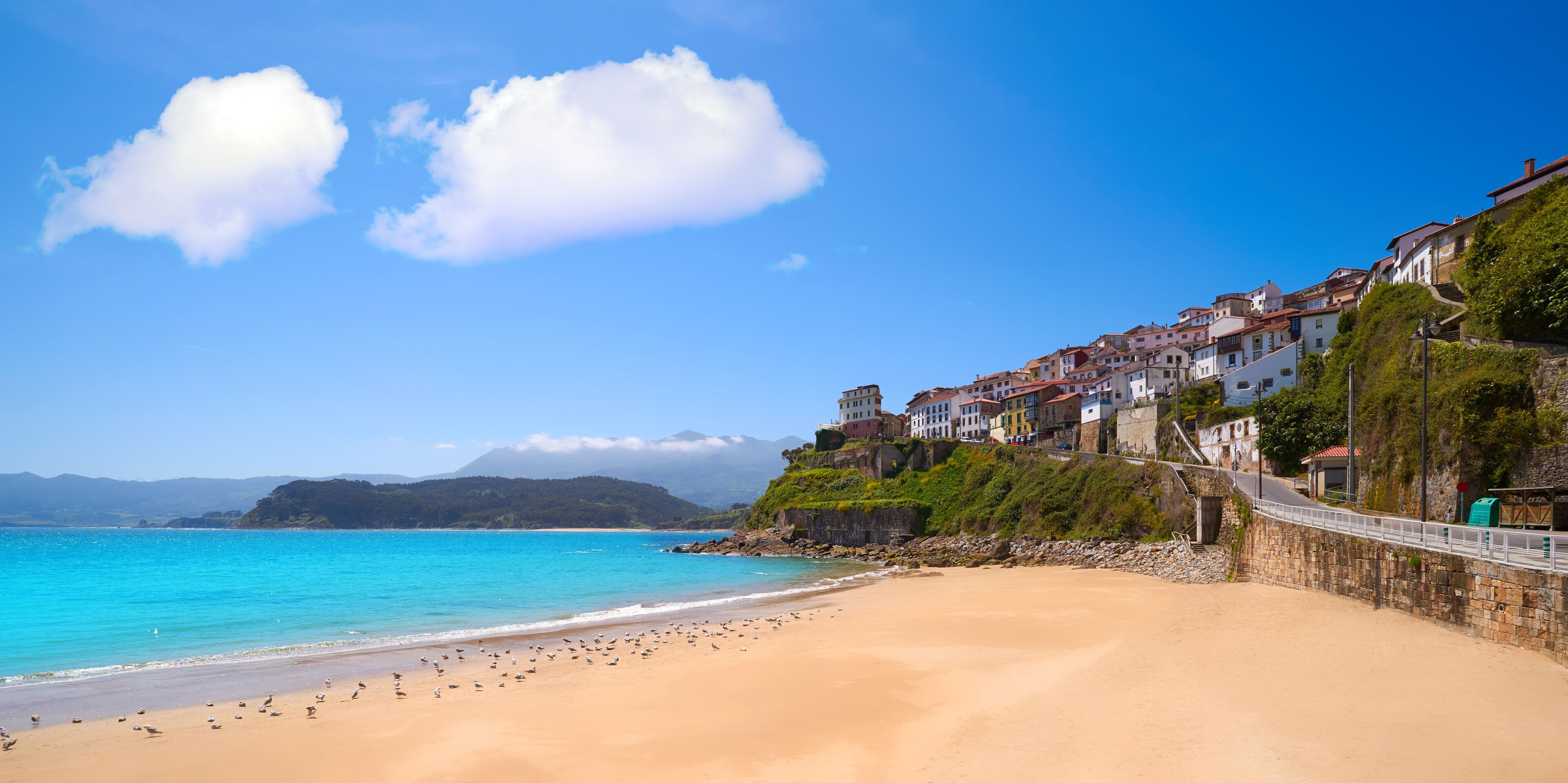 A coastal town with a sandy beach, a stone wall, and colorful buildings.