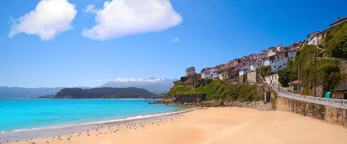 A coastal town with a sandy beach, a stone wall, and colorful buildings.