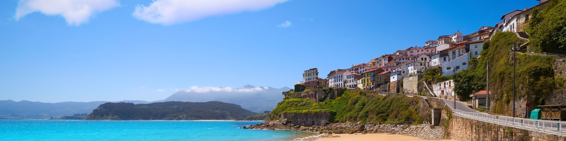A coastal town with a sandy beach, a stone wall, and colorful buildings.
