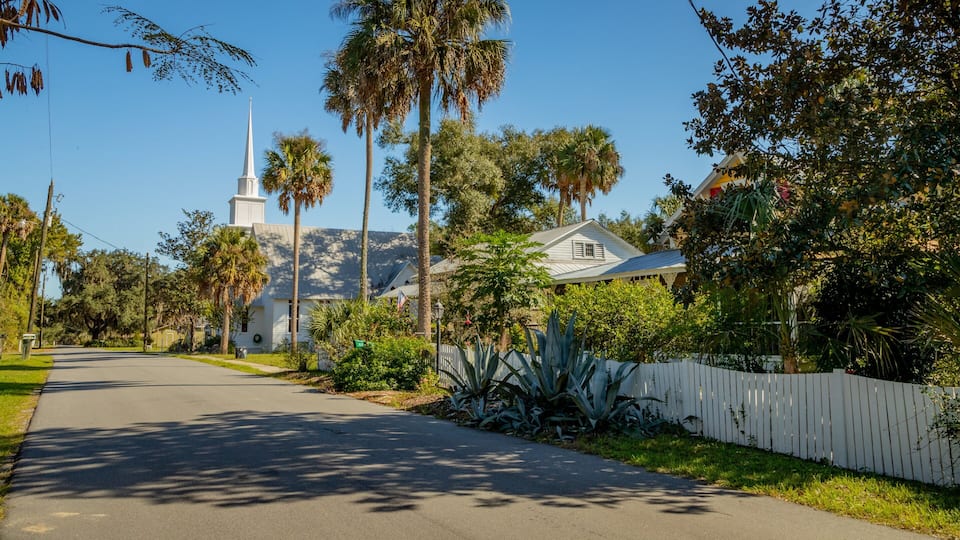A quiet street lined with palm trees and a church with a steeple.