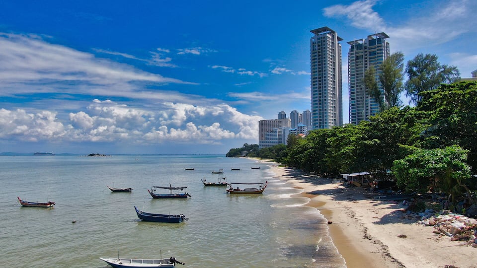A beach with boats, a sandy shore, and tall buildings in the background.