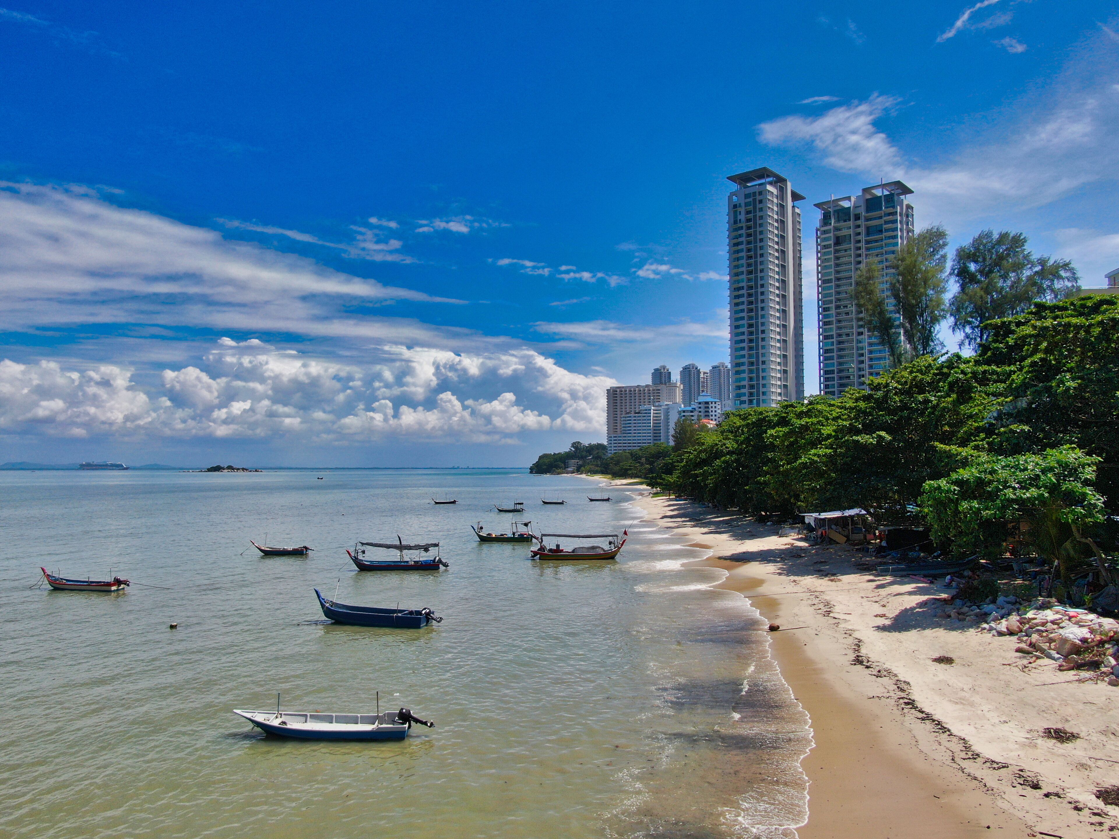 A beach with boats, a sandy shore, and tall buildings in the background.
