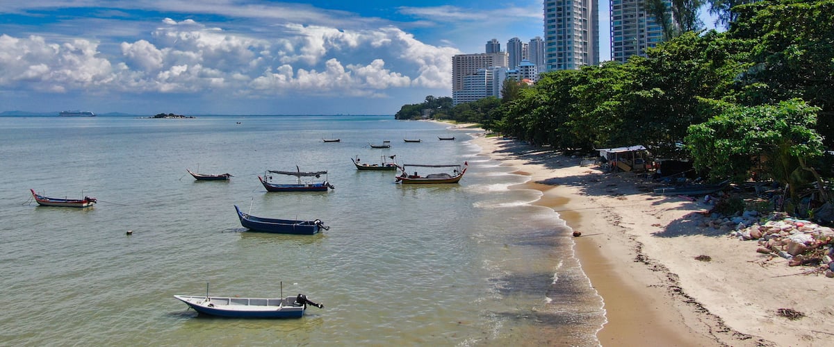 A beach with boats, a sandy shore, and tall buildings in the background.