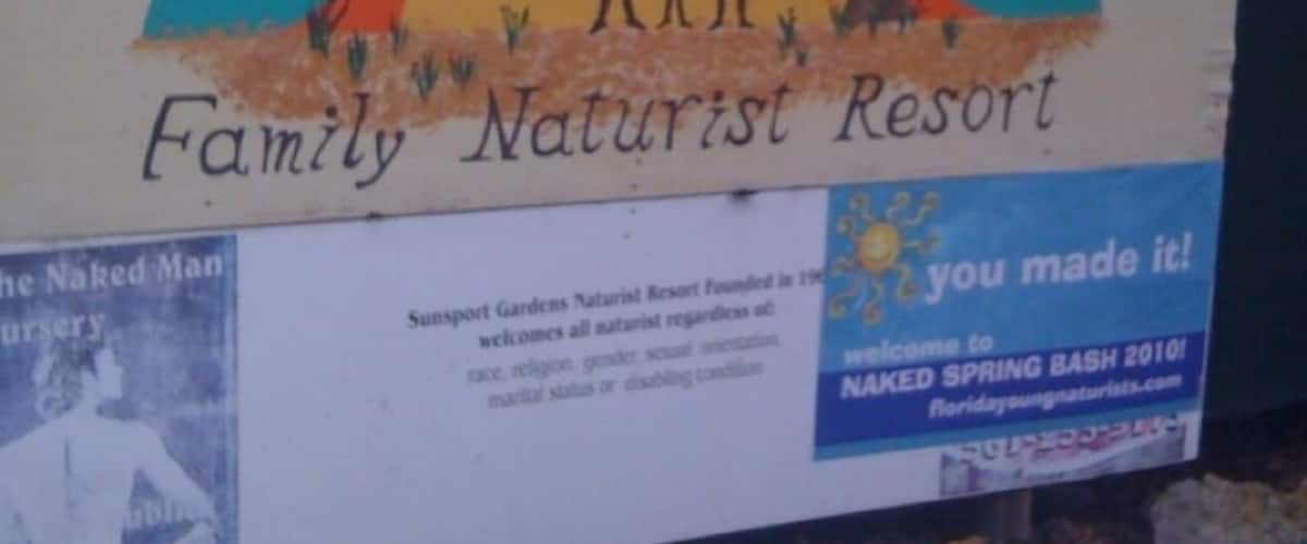 A sign for Sunport Gardens Family Naturist Resort with a sun and palm tree illustration.