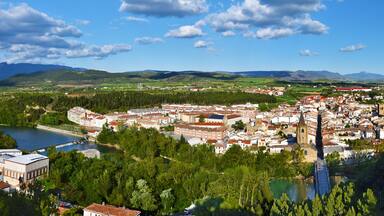 Un pueblo con un río, rodeado de montañas y vegetación.
