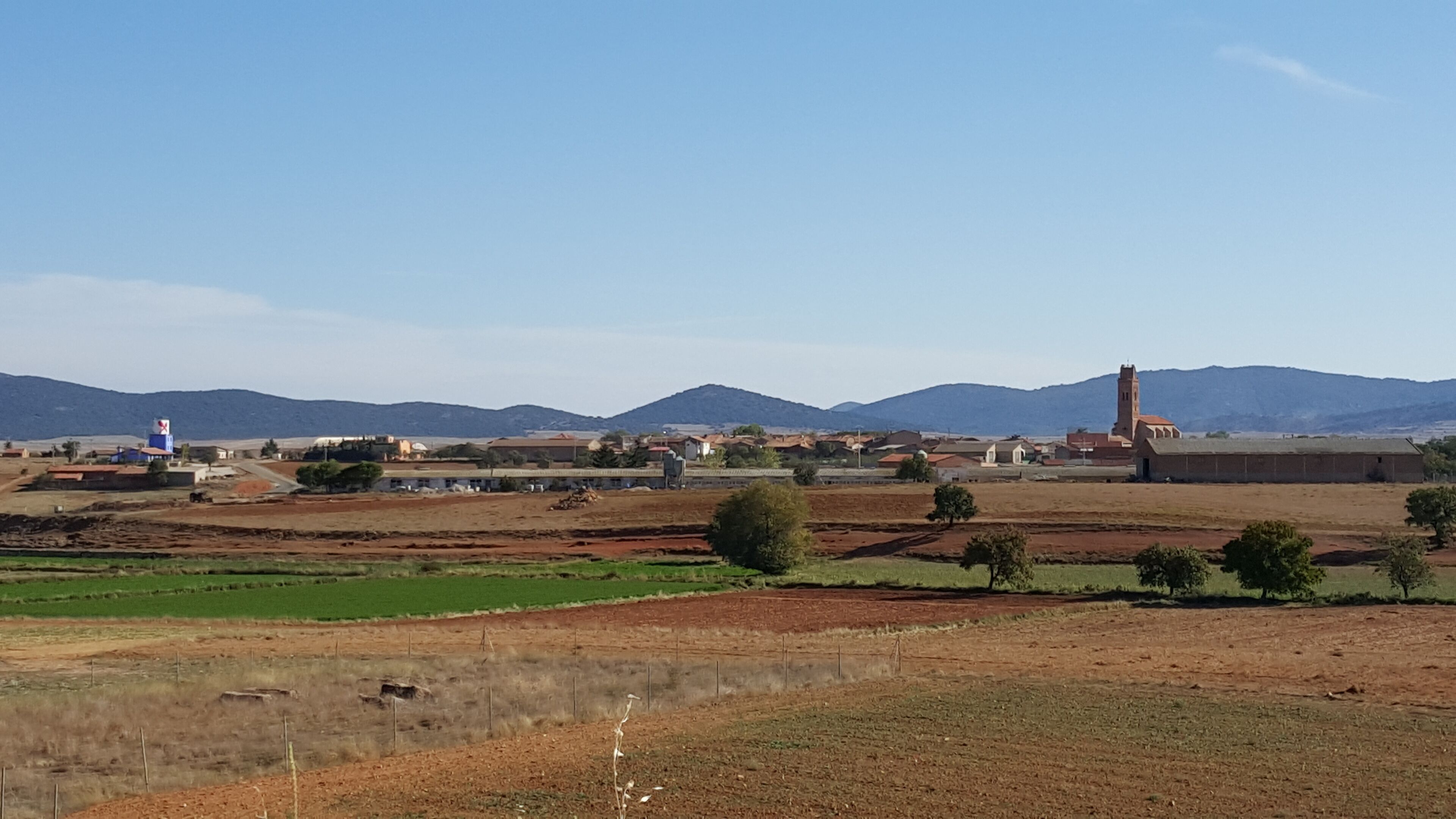 A rural landscape with fields, a water tower, and a church with a bell tower.