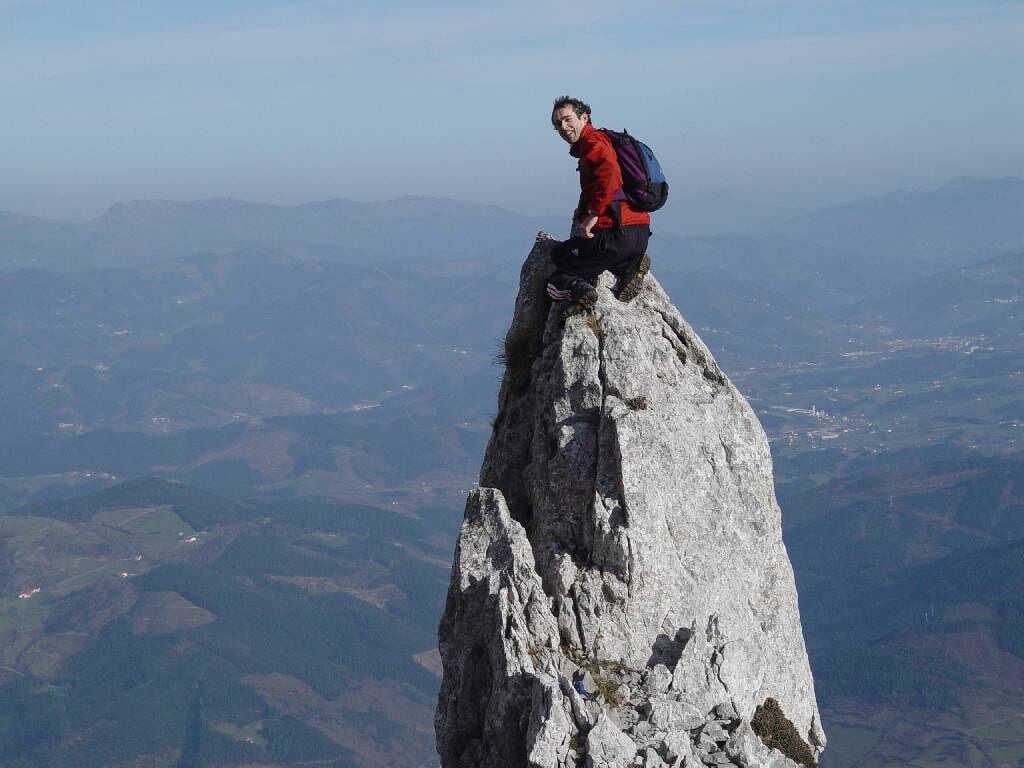 A person sitting on a rocky peak with a vast landscape in the background.