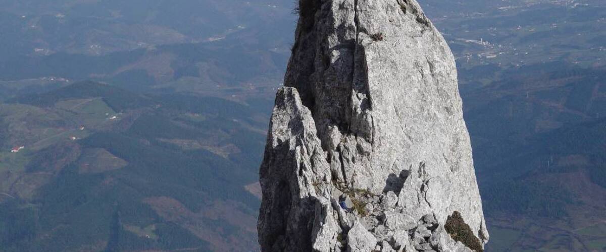 A person sitting on a rocky peak with a vast landscape in the background.