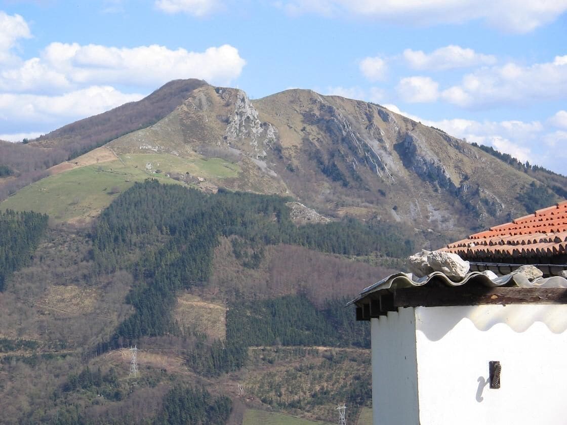 A mountain landscape with a white building in the foreground and a red-tiled roof.