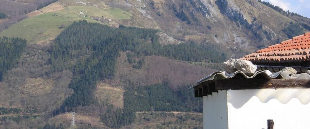 A mountain landscape with a white building in the foreground and a red-tiled roof.