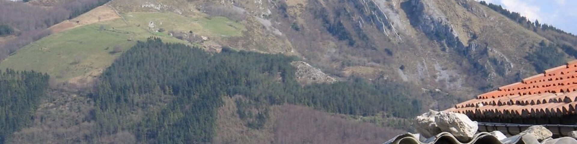 A mountain landscape with a white building in the foreground and a red-tiled roof.
